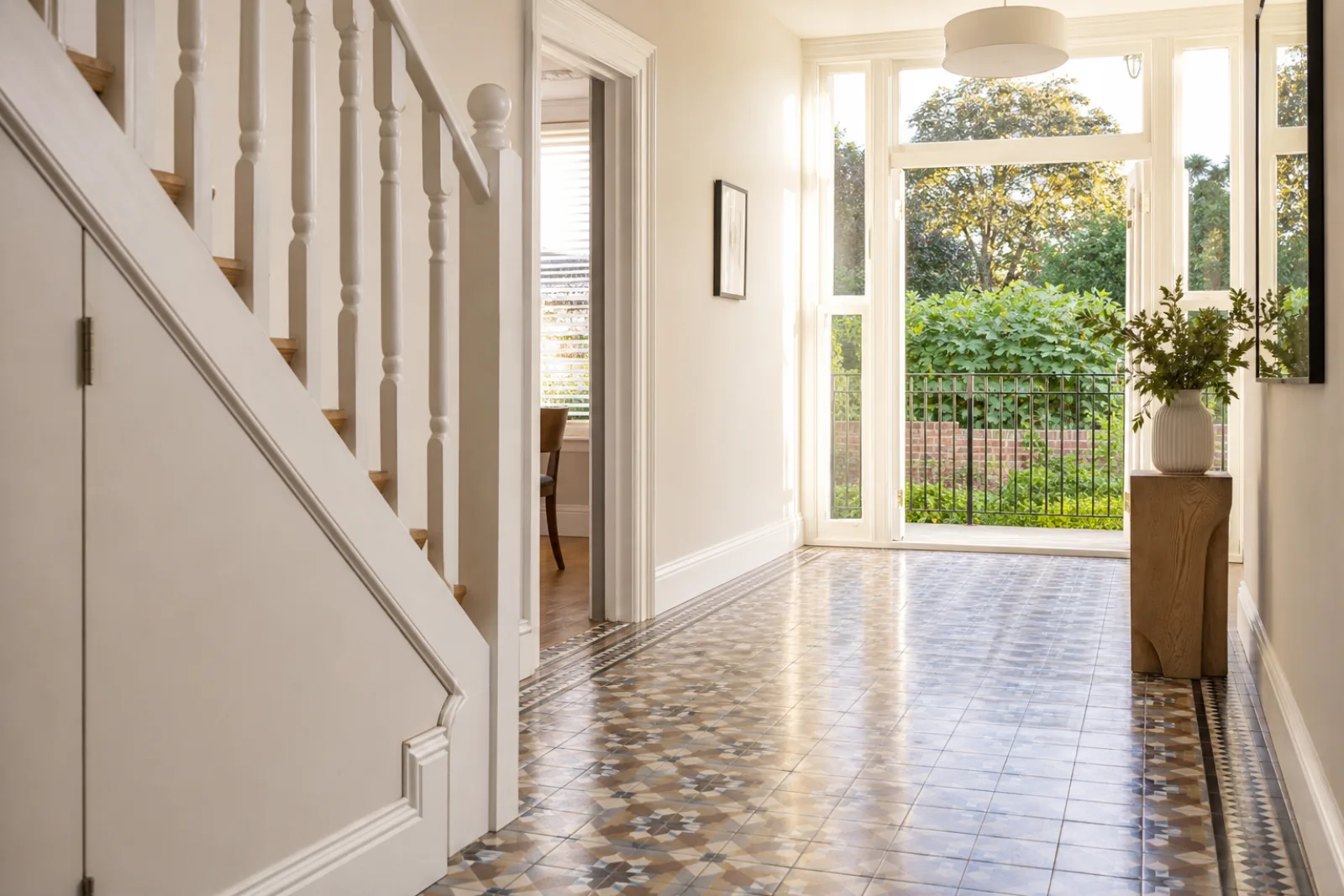 A freshly cleaned, spotless hallway with original tiled floor and white spindle staircase in a British modern apartment with floor-to-ceiling windows and a Juli