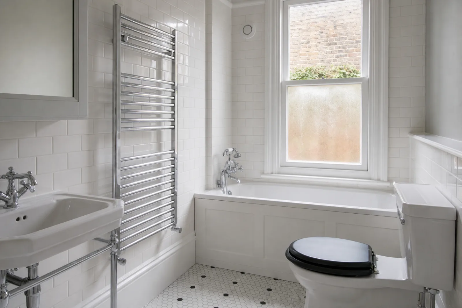 A pristine bathroom with white metro tiles and a gleaming chrome towel radiator in a British Victorian terraced house just after a professional clean, bright ov