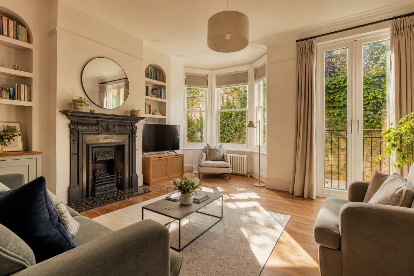 A freshly cleaned, spotless living room with a bay window and period fireplace in a British modern apartment with floor-to-ceiling windows and a Juliet balcony