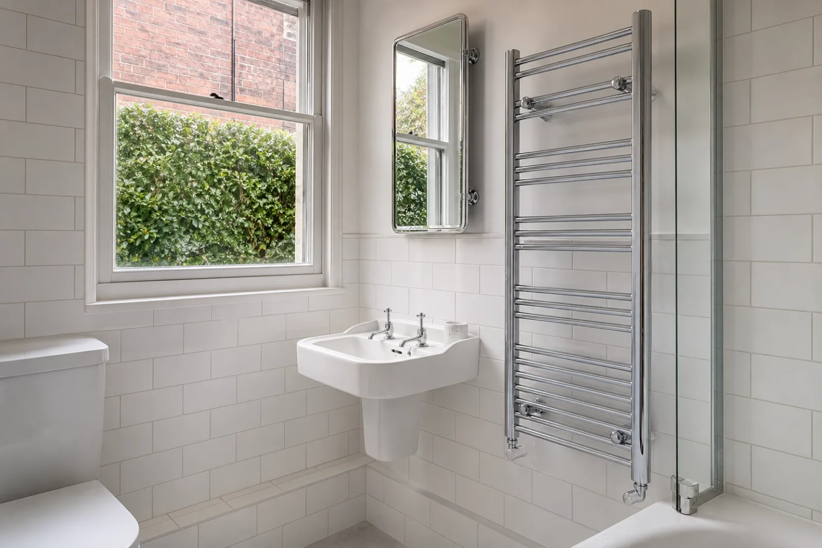 A pristine bathroom with white metro tiles and a gleaming chrome towel radiator in a British Victorian terraced house just after a professional clean