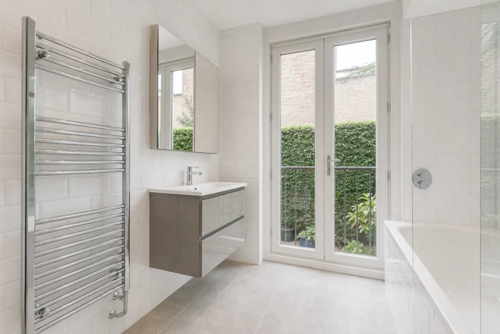 A bright, freshly cleaned bathroom with white metro tiles and a gleaming chrome towel radiator in a British modern apartment with floor-to-ceiling windows and a