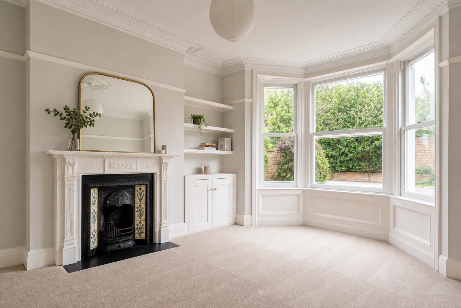 A bright, freshly cleaned living room with a bay window and period fireplace in a British Edwardian semi-detached house, bright overcast daylight
