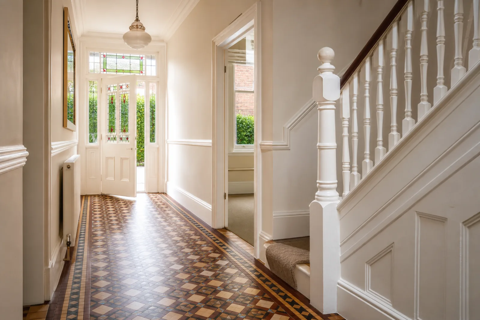 A freshly cleaned, spotless hallway with original tiled floor and white spindle staircase in a British Victorian terraced house