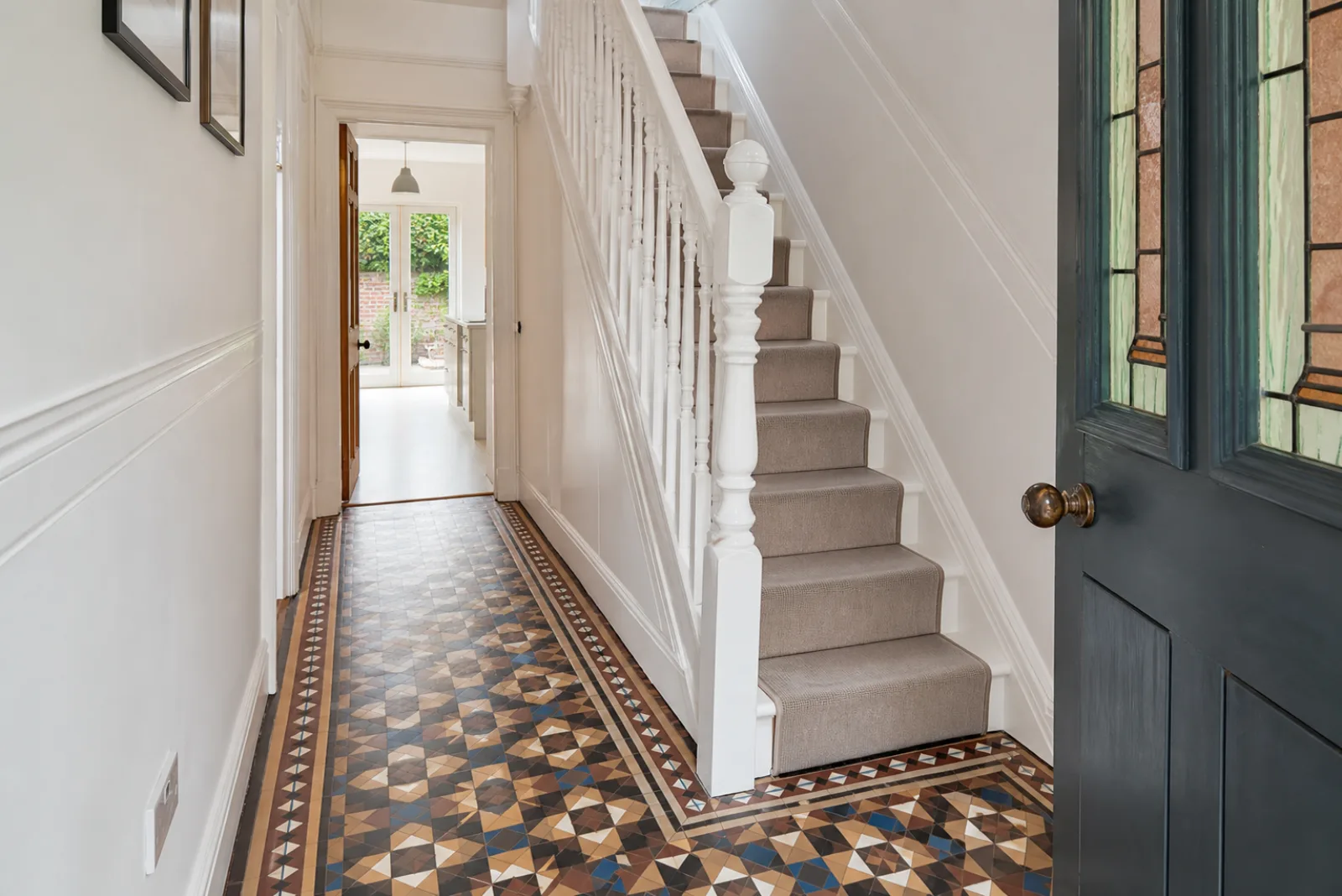 A pristine hallway with original tiled floor and white spindle staircase in a British Victorian terraced house just after a professional clean, bright overcast 