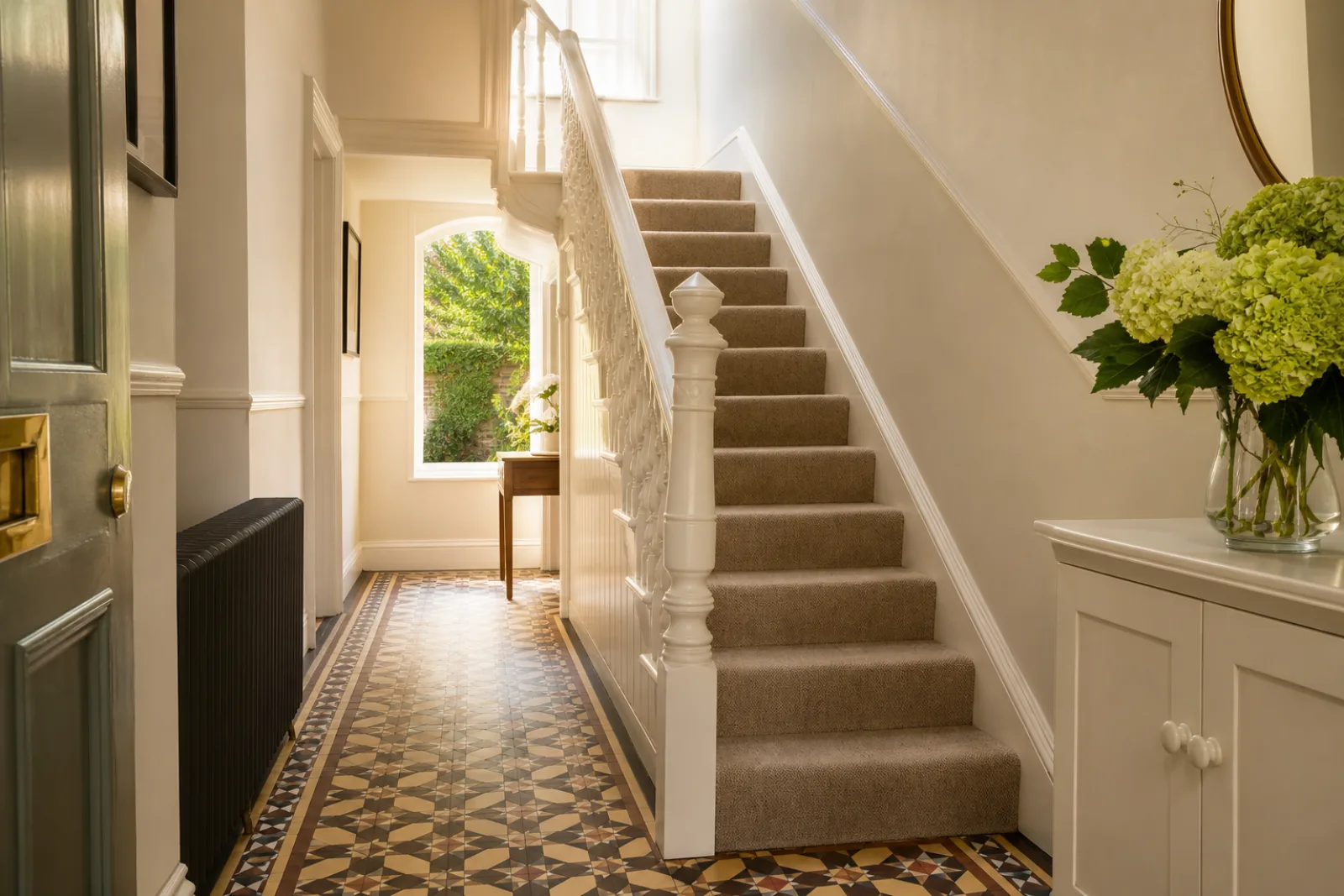 A freshly cleaned, spotless hallway with original tiled floor and white spindle staircase in a British Victorian terraced house