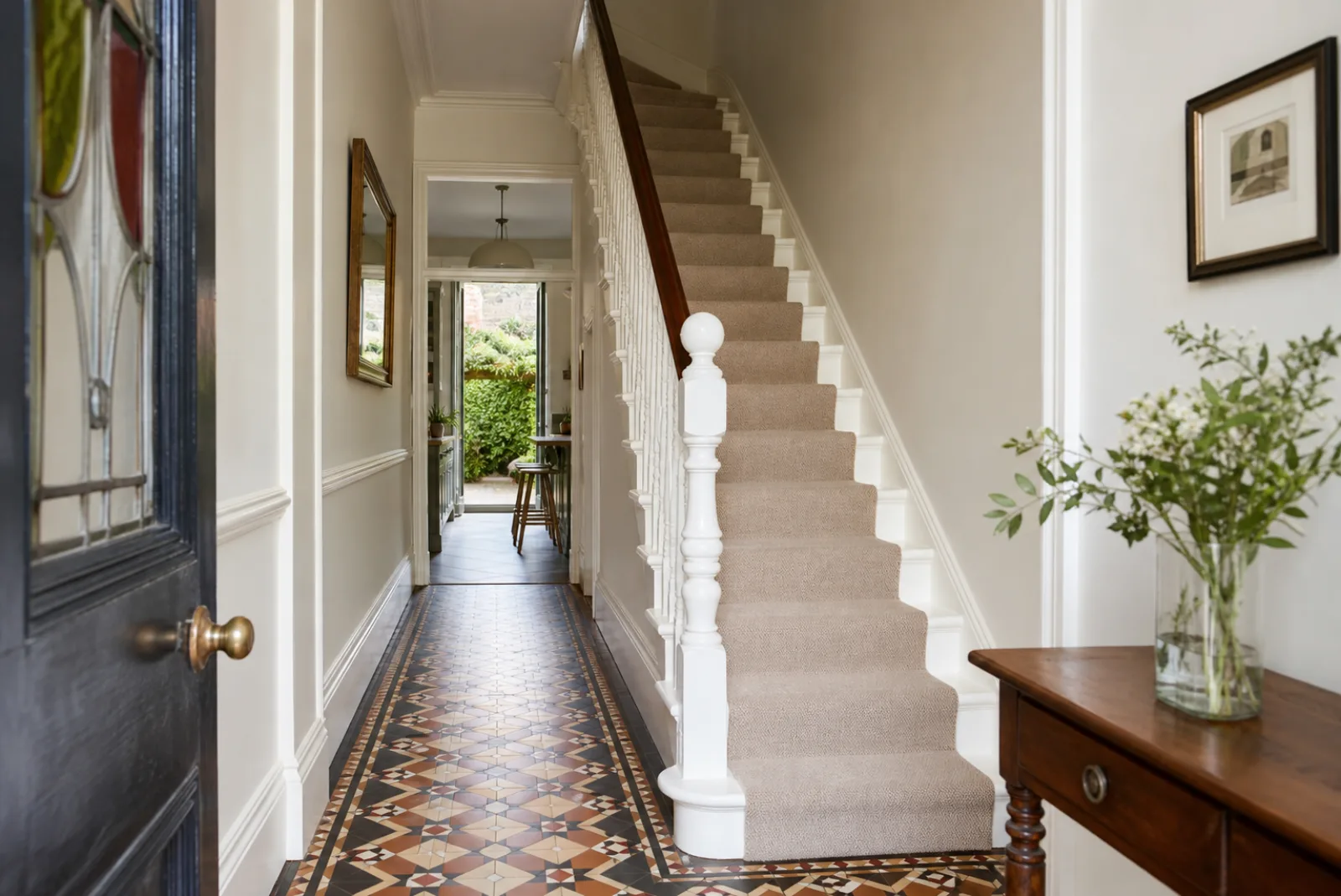A pristine hallway with original tiled floor and white spindle staircase in a British Victorian terraced house just after a professional clean