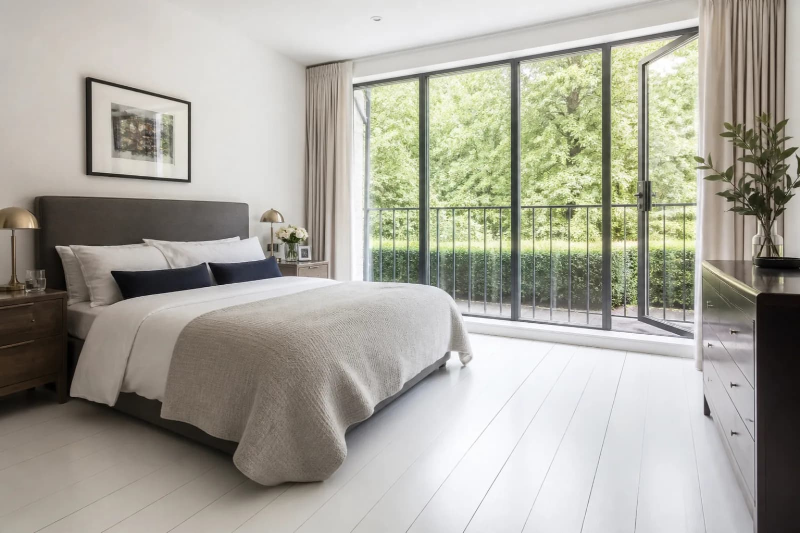 A freshly cleaned, spotless bedroom with painted floorboards and a neatly made bed in a British modern apartment with floor-to-ceiling windows and a Juliet balc