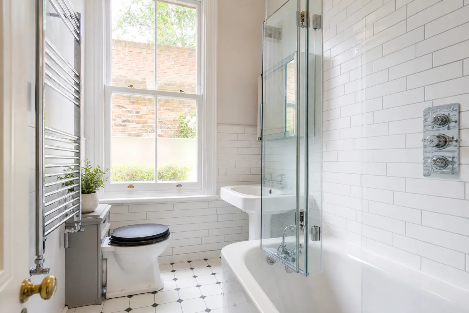 A pristine bathroom with white metro tiles and a gleaming chrome towel radiator in a British Edwardian semi-detached house just after a professional clean, brig