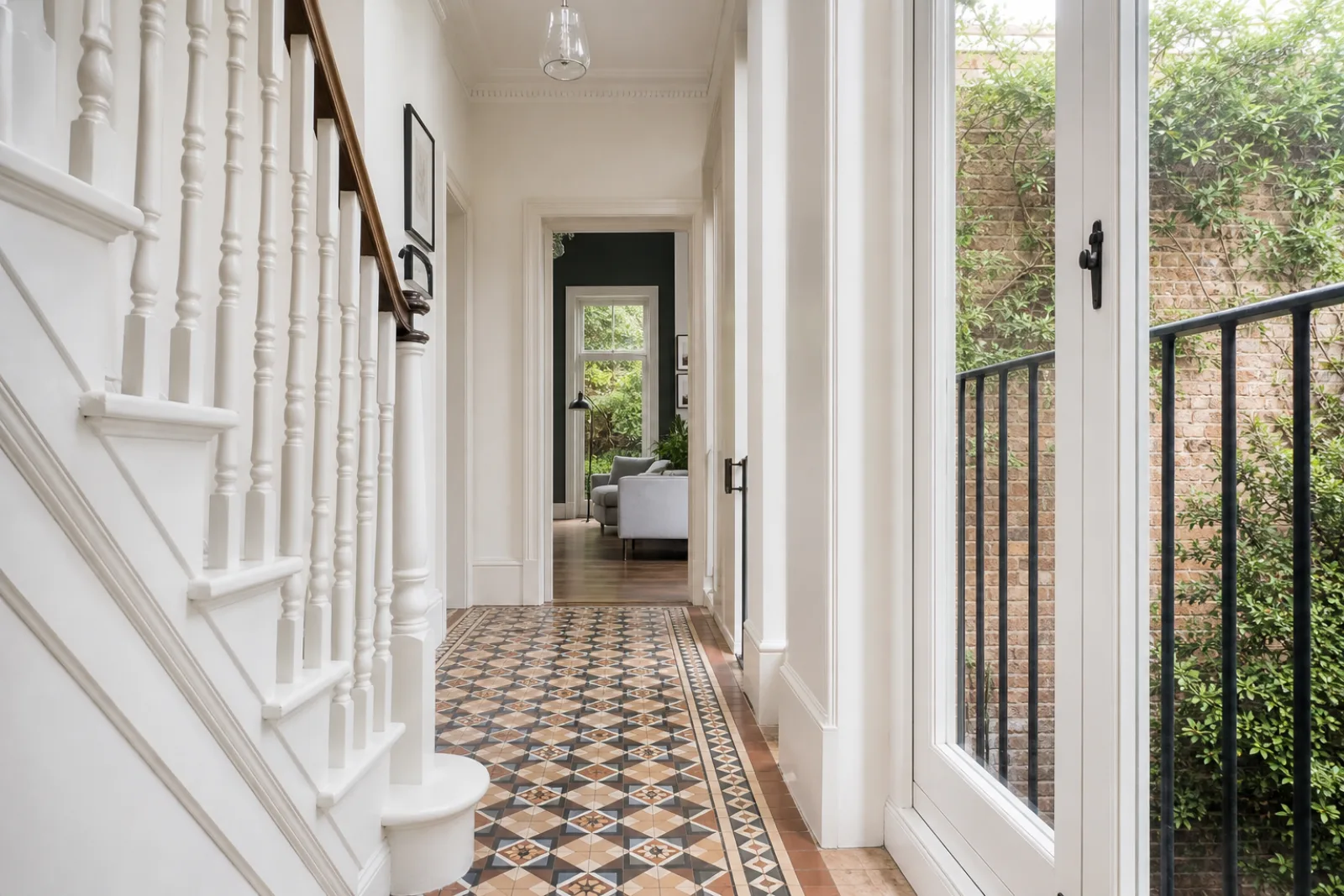 A pristine hallway with original tiled floor and white spindle staircase in a British modern apartment with floor-to-ceiling windows and a Juliet balcony just a