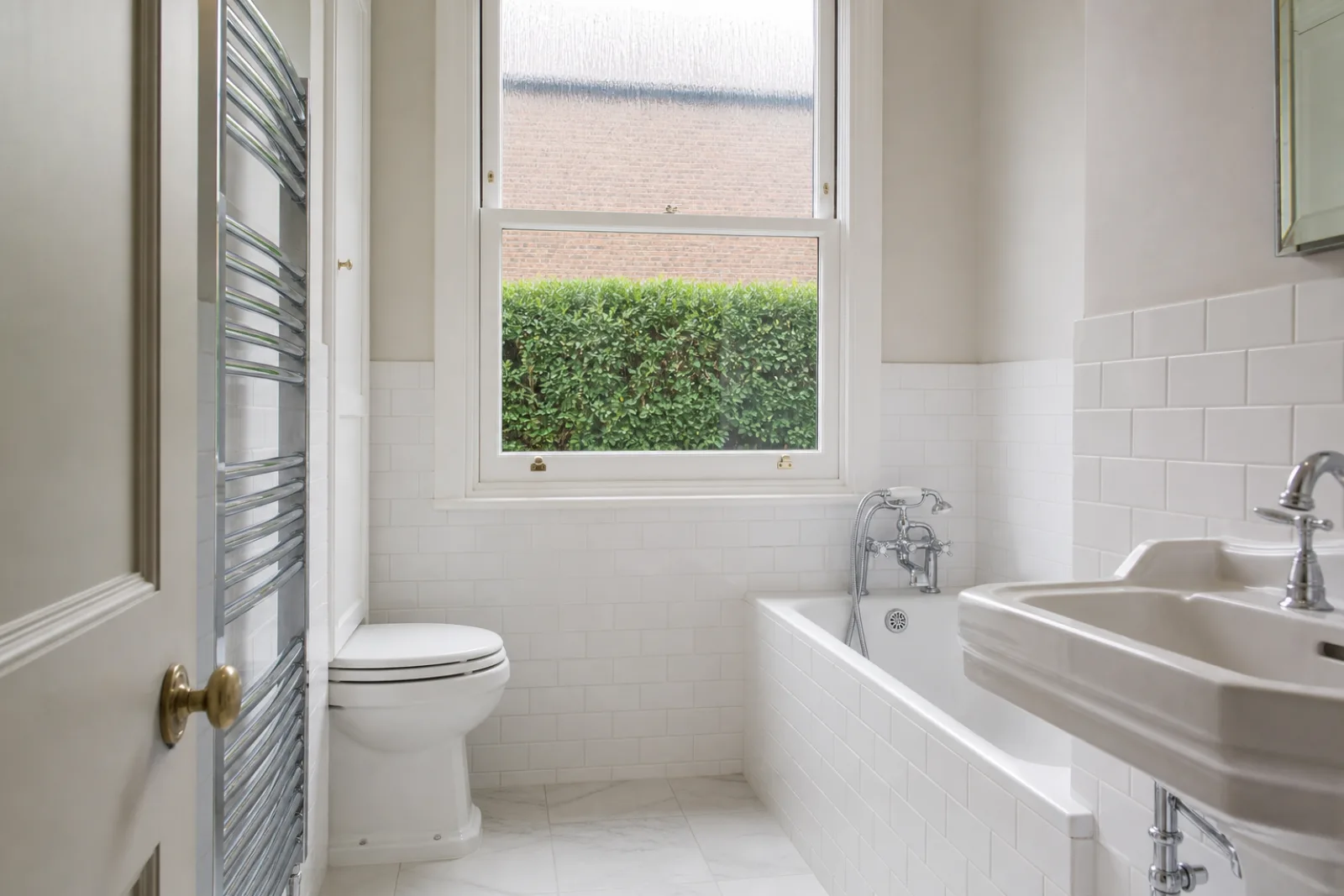 A pristine bathroom with white metro tiles and a gleaming chrome towel radiator in a British Edwardian semi-detached house just after a professional clean, brig