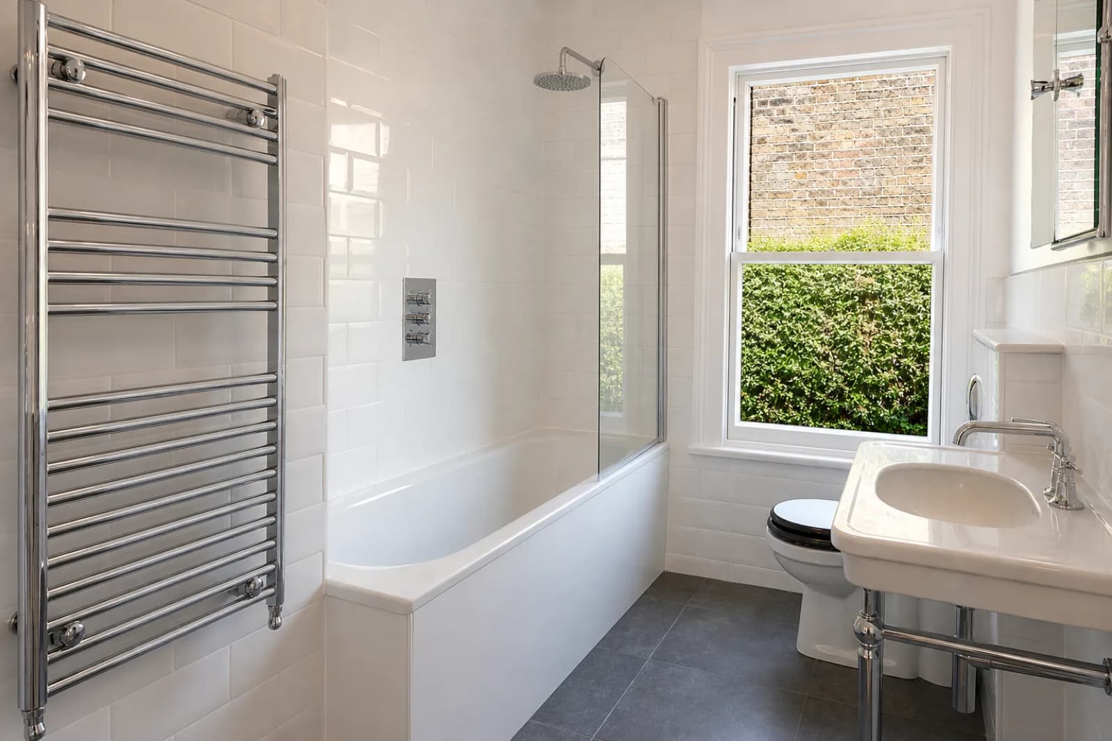 A pristine bathroom with white metro tiles and a gleaming chrome towel radiator in a British Victorian terraced house just after a professional clean