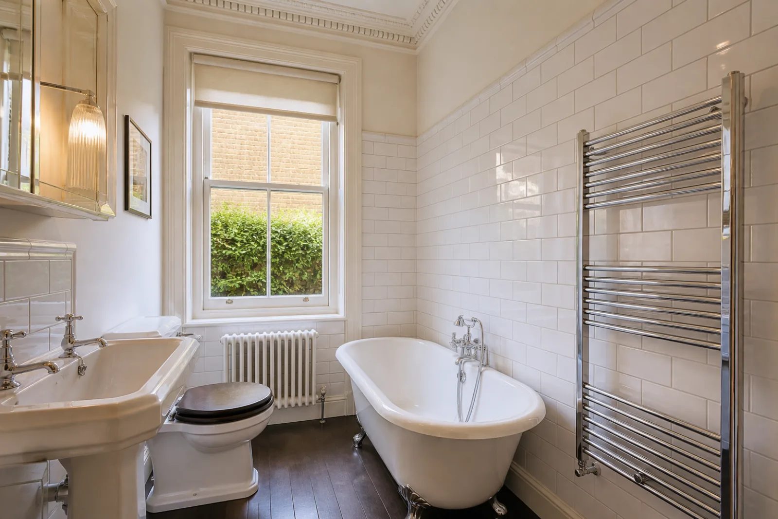 A freshly cleaned, spotless bathroom with white metro tiles and a gleaming chrome towel radiator in a British converted period flat with high ceilings and corni
