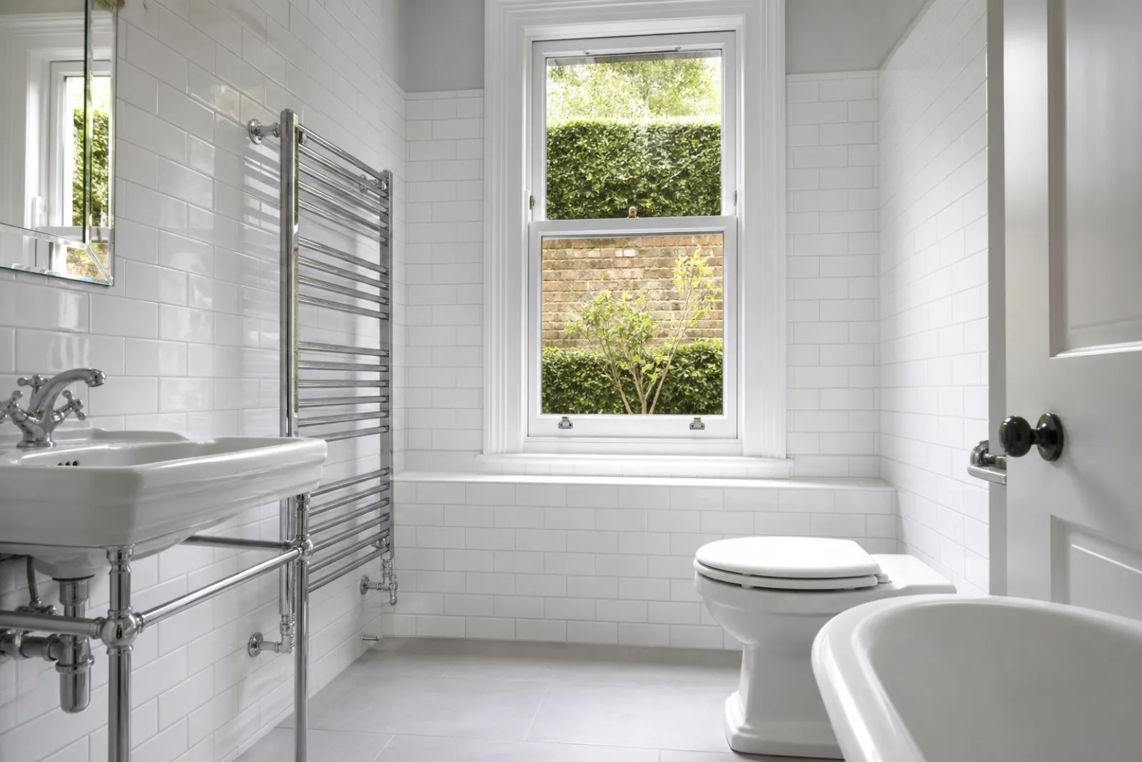 A pristine bathroom with white metro tiles and a gleaming chrome towel radiator in a British Edwardian semi-detached house just after a professional clean, brig