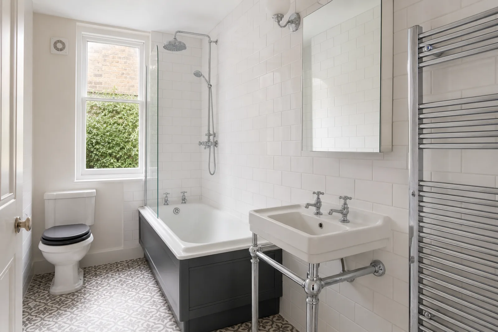 A pristine bathroom with white metro tiles and a gleaming chrome towel radiator in a British Victorian terraced house just after a professional clean, bright ov